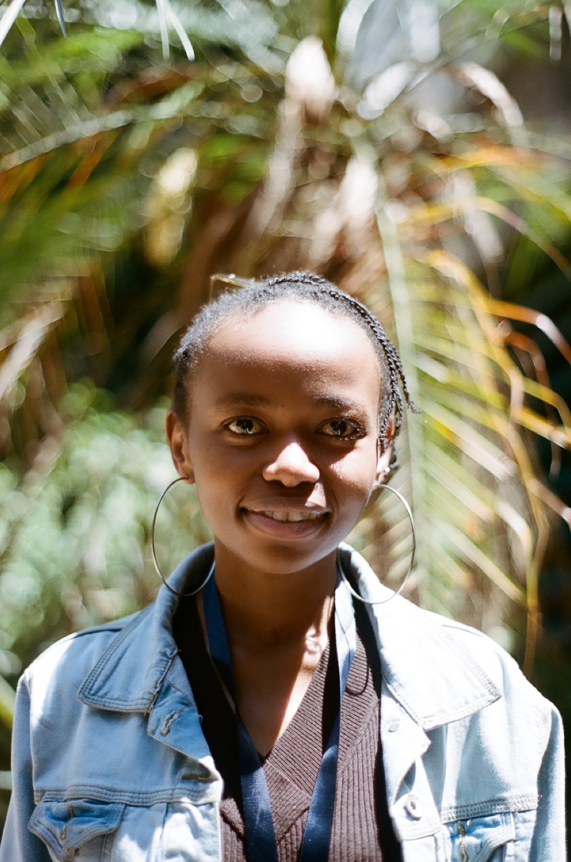 Photo portrait of young African woman smiling with short braids, big hoop earings and a jean jacket.