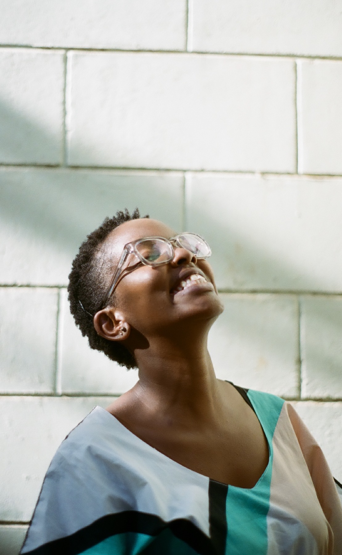 Photo portrait of young African woman smiling with short hair and glasses looking up.