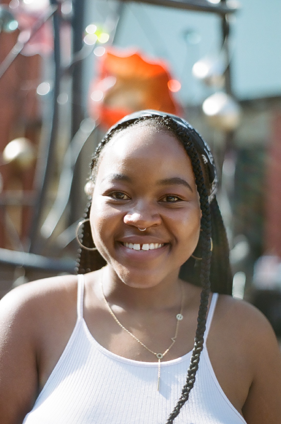 Photo portrait of young African woman smiling with braids and a nose ring, wearing a white top.