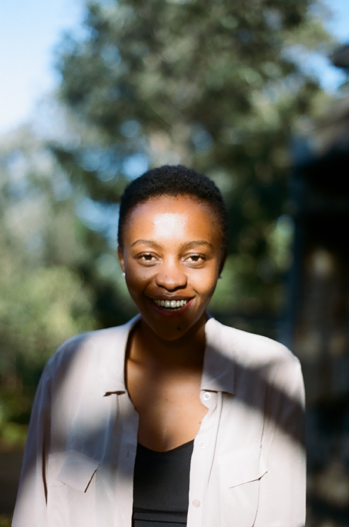Photo portrait of young African woman smiling with short haird and a white blouse on top of a black top.