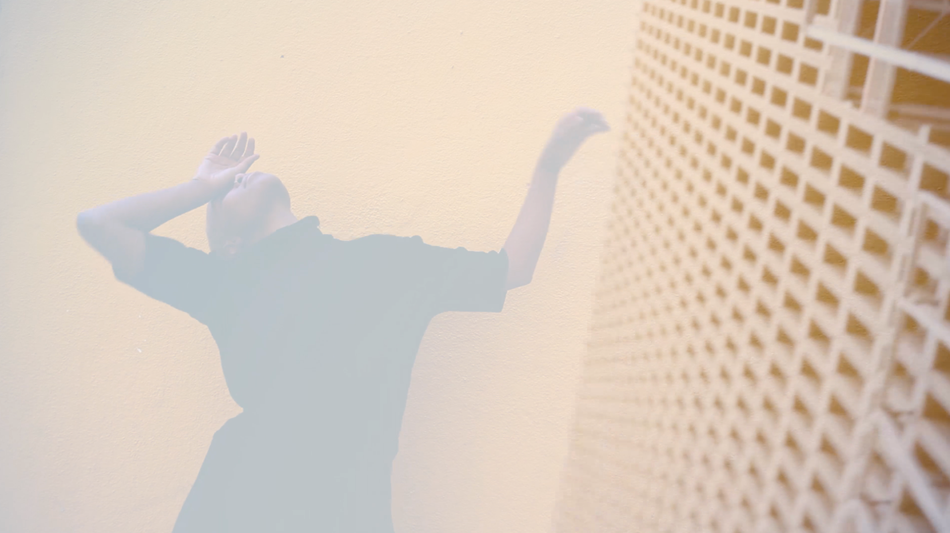 Still image from Ode to an Architect film showing the main protagonist dancing silhouette overlayed on a building seen from the below on the street. The colours are pale yellows, grey and brown.