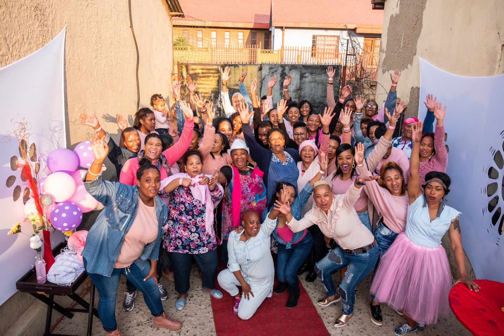 Women of Westbury posing with their hands raised high, smiling and all wearing pink
