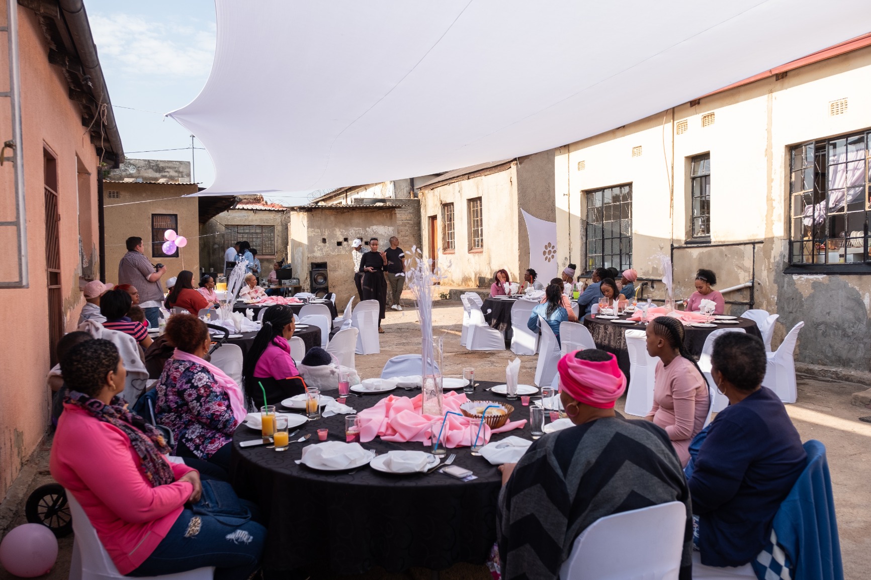 Photo of women seated at the lunch tables in the courtyard watching Khensani Jurczok-de Klerk give a talk.