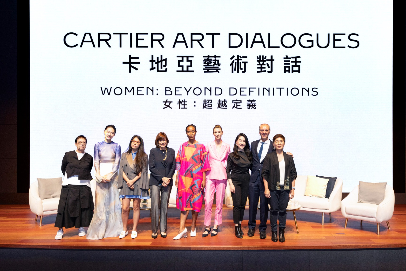 Group photo of some participants from the panel discussions standing on stage. The colours are pink, black, white and other warm tones.